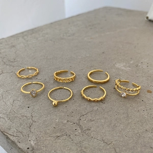 Set of 7 gold-finished S925 silver rings with zircon inlay on minimalist stone surface