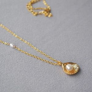 Macro detail of gold shell pendant with pearl inlay on a minimalist brass necklace