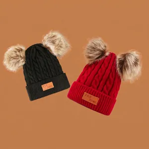 Red and black knit children's beanies with two large faux fur pom poms and leather patches