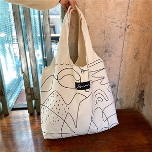 Detail of white canvas tote bag featuring abstract black line art and minimalist patch