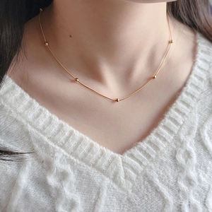 Close-up of elegant rose gold beaded snake chain necklace worn on white knit sweater