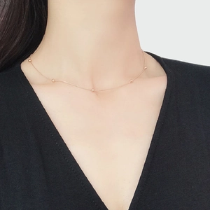 Close-up of minimalist rose gold snake chain necklace with five beads on a female model