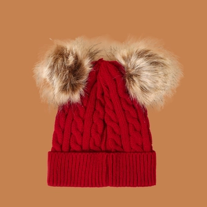 Close-up of red knit hat featuring double brown pom-poms and classic cable patterns