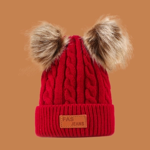 Detail of red knit kids hat with two brown pom-poms and leather logo patch