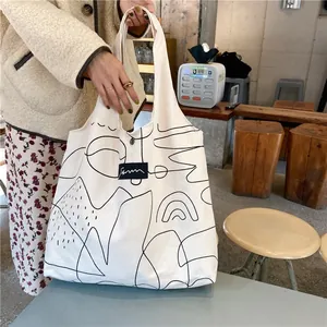 Close-up of white canvas tote bag with black abstract line art and sturdy shoulder straps