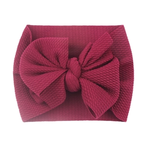 Close-up of wine red knitted baby headband with a large bow on white background
