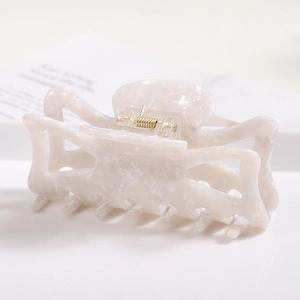 Macro view of a large white acetate hair claw clip with elegant marble texture and gold spring