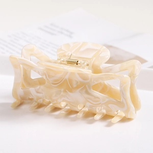 Close-up of cream marble texture hair claw clip with golden spring on a white tray