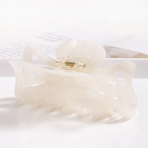 Close-up of cream white acetate hair claw clip showing glossy finish and gold metal spring