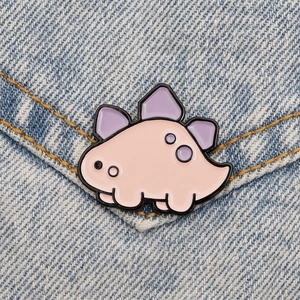 Close-up of a cute pink and purple enamel dinosaur pin on a blue denim jacket