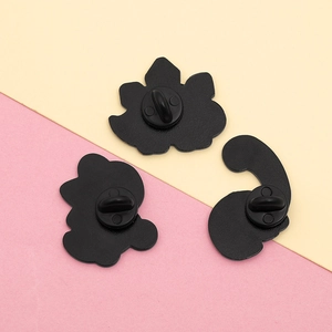 Detail of matte black butterfly clutches and enamel pin backs on a pastel background