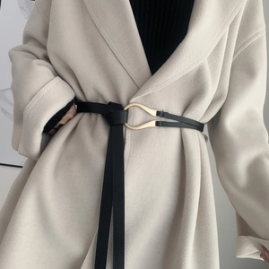 Close-up of a slim black leather belt with a U-shaped gold buckle on a beige wool coat