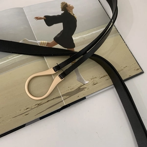 Detail of black lychee texture leather belt featuring a polished golden horseshoe buckle