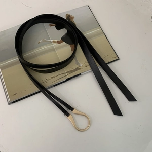 Detail of a thin black leather belt with a matte gold horseshoe buckle on a magazine