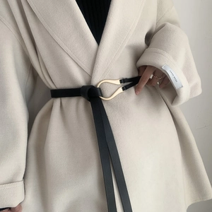 Slim black leather belt with golden horseshoe buckle styled on an off-white wool coat