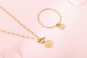 Détail de pendentifs pièces dorées et chaînes trombones sur collier et bracelet