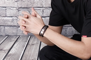 Close-up of a men's punk leather bracelet with a silver skull charm worn by a model