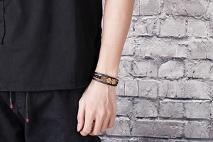 Macro detail of men's multilayer black leather bracelet with three bronze skull charms