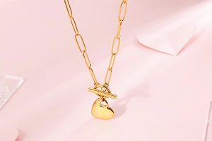 Close-up of golden paperclip chain necklace with heart pendant and OT clasp on pink background
