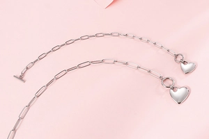 Flat lay of silver heart necklaces with toggle clasp on pink silk background