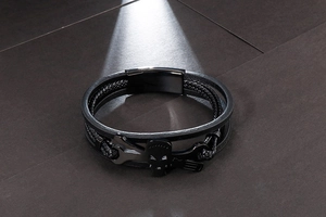 Detail of men's black braided leather bracelet with skull and wrench metal charms