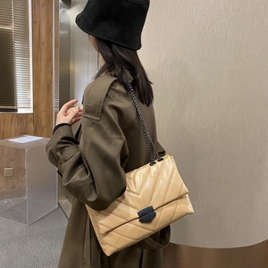 Chic beige quilted crossbody bag with V-shaped stitching and black chain strap worn on coat