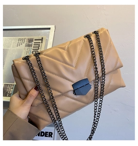 Detail of khaki V-quilted chain bag with metallic hardware held against textured wall