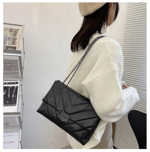 Detail of a large black V-quilted shoulder bag with dark metal chain on a model