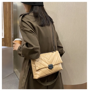 Detail of beige quilted shoulder bag with V-shaped stitching and dark metal chain strap