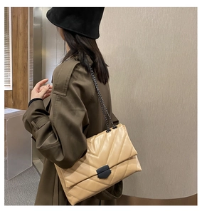 Detail of beige quilted shoulder bag with V-shaped stitching and black chain strap