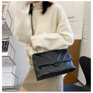 Detail of black quilted crossbody bag with V-shaped stitching and metal chain strap