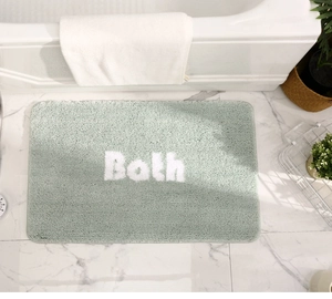 Detailed view of soft light green bath mat with Bath text on marble bathroom floor