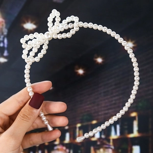 Detail of handmade faux pearl headband with elegant bow knot held by a hand