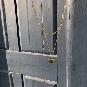 Detail of double-layer gold necklace with angel relief pendant and paperclip chain