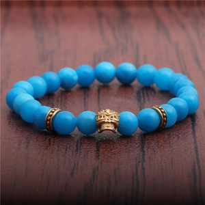 8mm blue agate bead bracelet featuring a gold skull charm on a dark wooden background