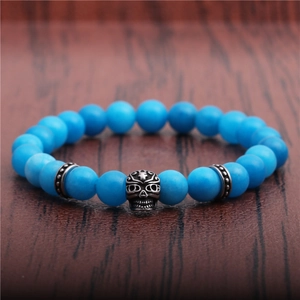 Macro detail of 8mm blue agate beads and silver skull charm on a beaded bracelet