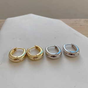 Detail of high-polish oval huggie earrings in gold and silver finishes on stone base