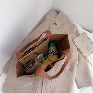 Brown leather tote bag with large capacity and stitch detail shown on beige coat