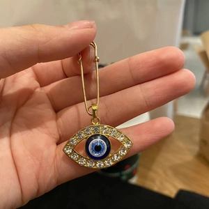 Close-up of golden evil eye brooch pin featuring blue crystal accents in a hand-held view