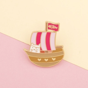 Detail van een emaille speld met een roze gestreept piratenschip en een witte kat op de boeg