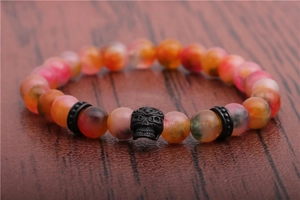 Macro detail of 8mm multicolored agate beads and black skull charm on wooden surface