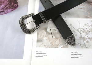 Macro detail of retro engraved silver buckle and tip on a black leather belt