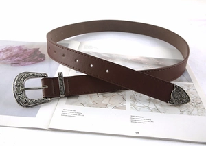 Detail of vintage carved silver buckle on a brown leather belt with western styling