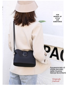 Detailed view of black crossbody bag with round metal buckle worn on the shoulder