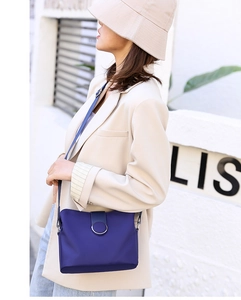 Blue mini crossbody phone bag with round metal buckle worn over a beige blazer