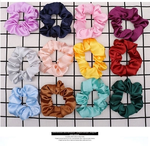 Flat lay of 12 multi-colored satin hair scrunchies on a checkered background