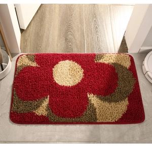 Detail of plush rectangular doormat with red and beige floral patterns on tile floor