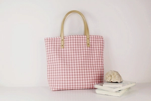 Detail of pink gingham canvas tote bag with leather handles and gold rivet accents