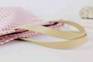 Detailed close-up of pink checkered canvas tote bag leather handles and fine stitching