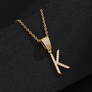 Golden letter K pendant necklace with pave-set cubic zirconia on a black leather background